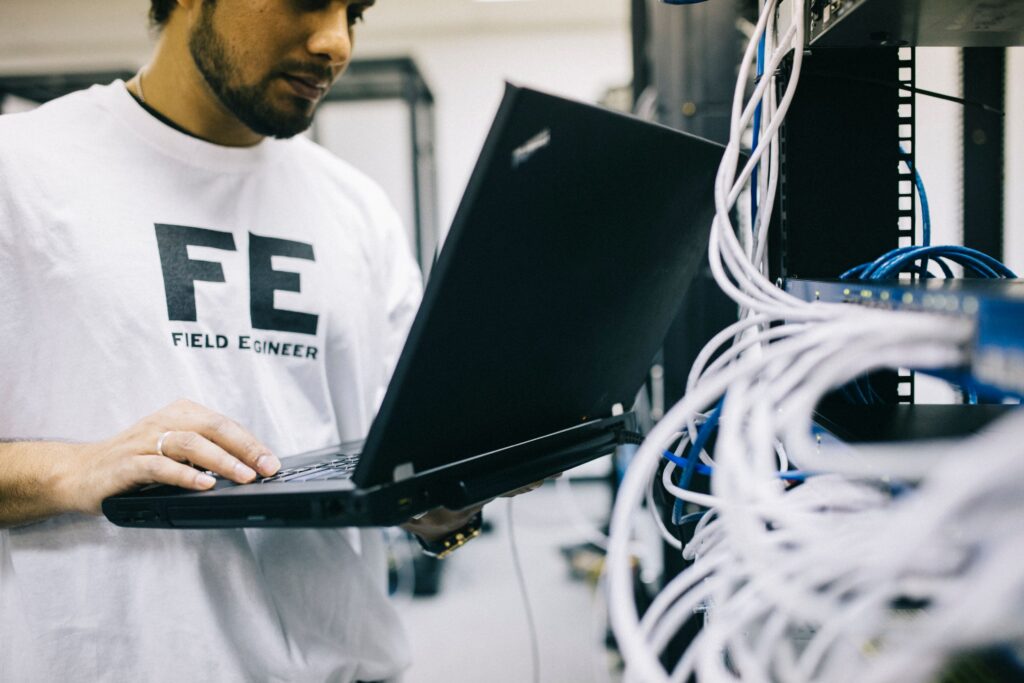 IT-Techniker arbeitet mit Laptop an Netzwerkinfrastruktur für sicheren und planbaren Betrieb.